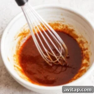 A bowl of sauce with a whisk in it, depicting the marinade preparation.