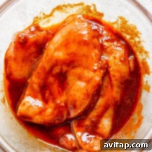 Chicken in a bowl covered with the BBQ marinade, ready for marinating.