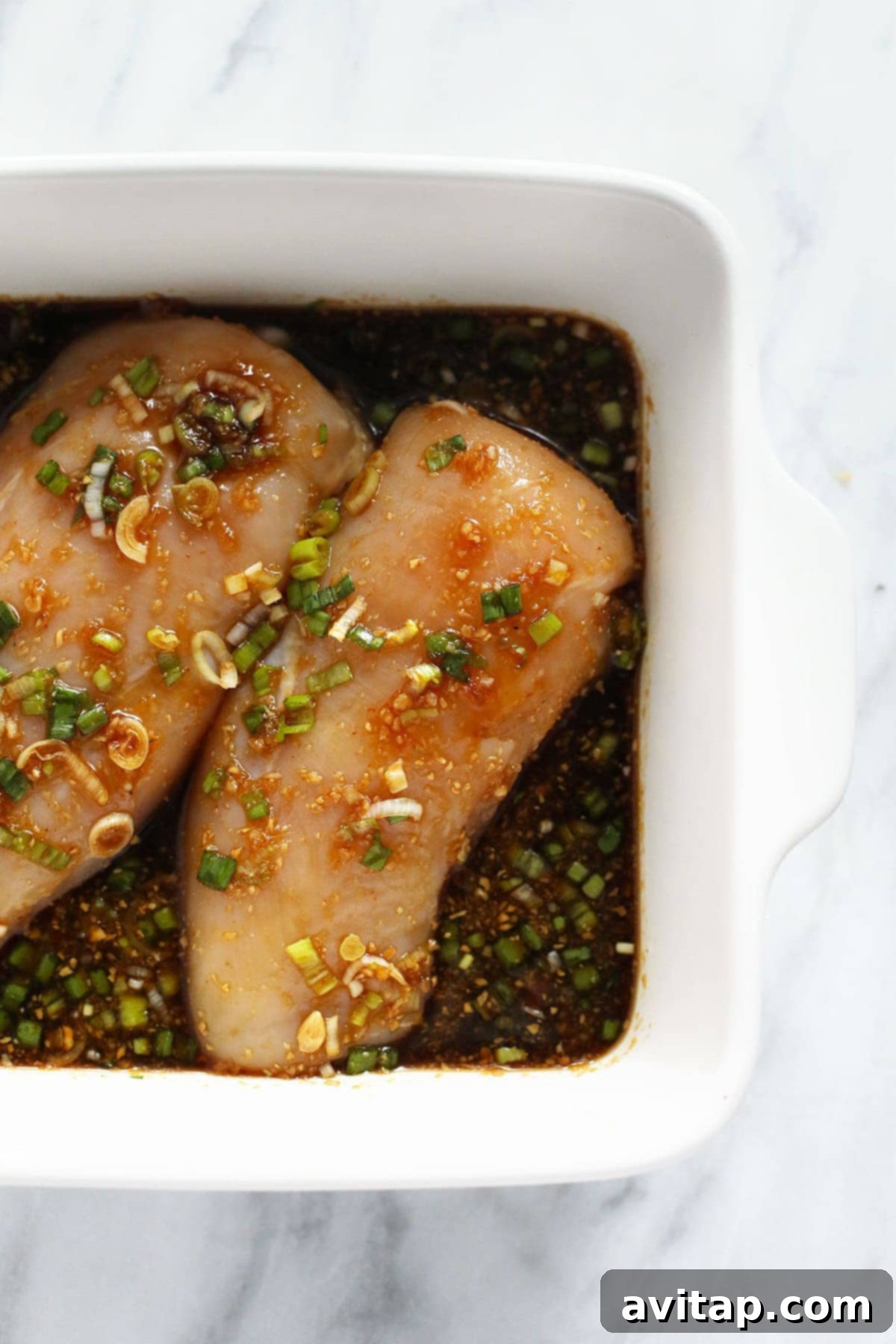 Two chicken breasts marinating in a flavorful teriyaki sauce