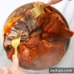 A person using a fork to shred tender pulled pork, highlighting the cooking success.