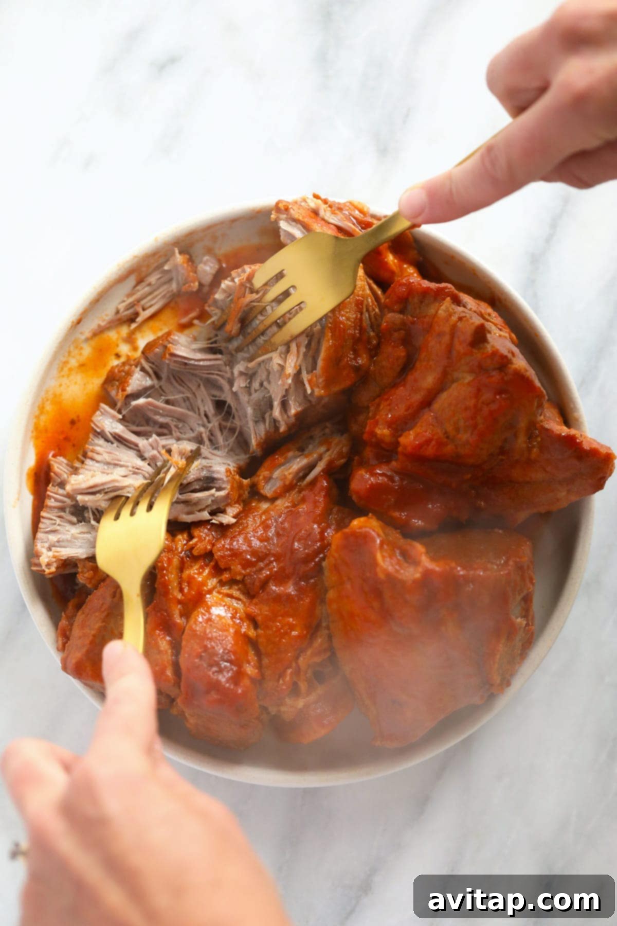 Shredding perfectly cooked pork with two forks on a cutting board, ready to be added back into the chili.