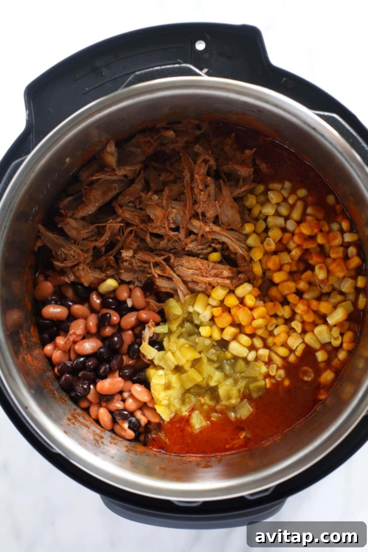 Various ingredients for Instant Pot Pork Chili, including pork, seasoning, beans, and tomatoes, placed inside the pressure cooker.