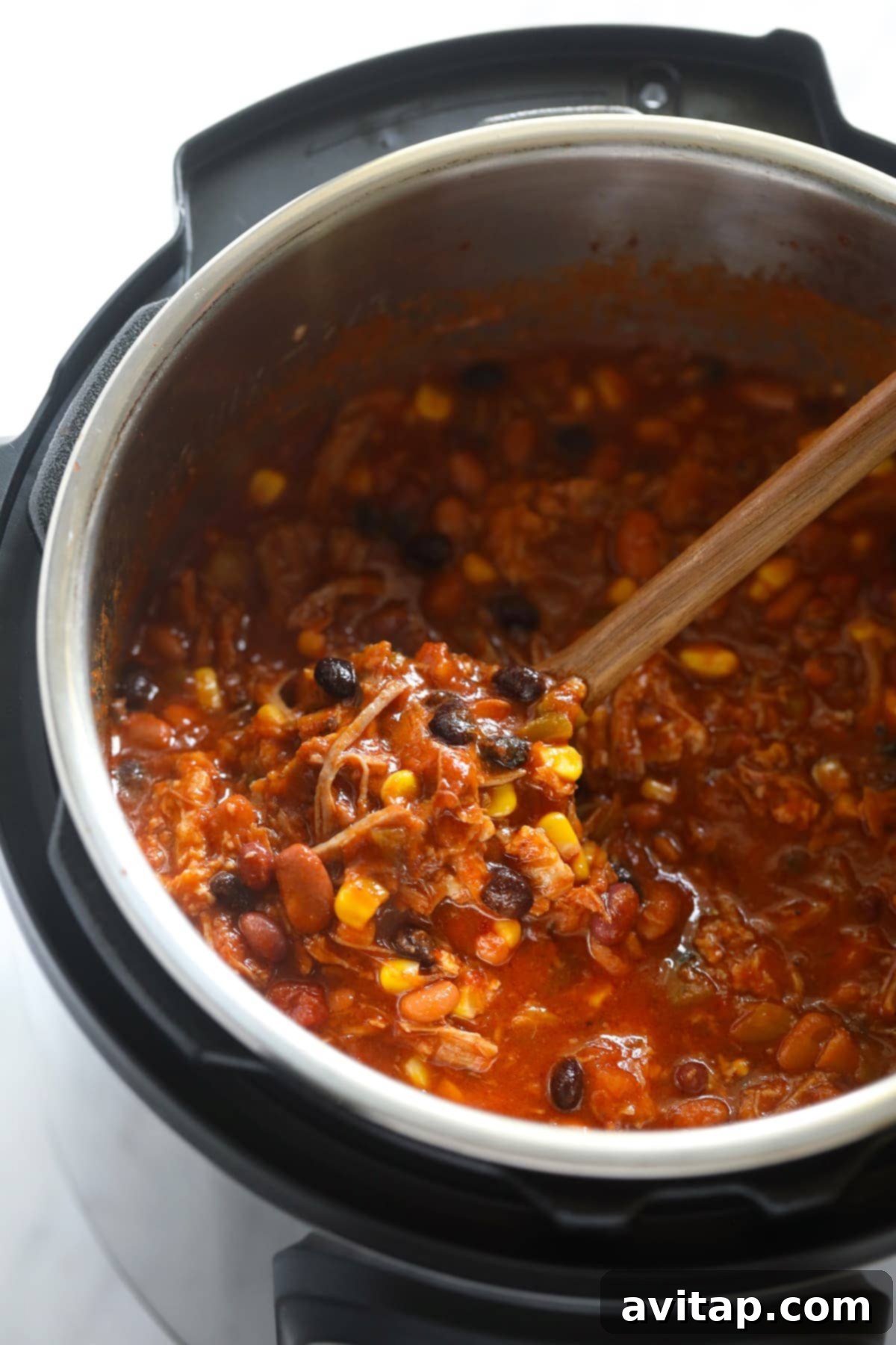 A large Instant Pot filled with delicious pulled pork chili and a serving spoon, ready to be dished out.
