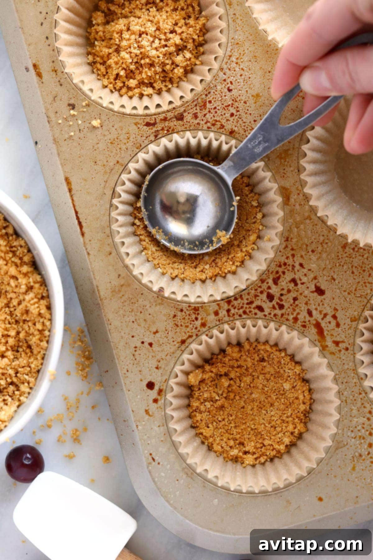Pressing graham cracker crust into muffin tins for cranberry cheesecake bites.