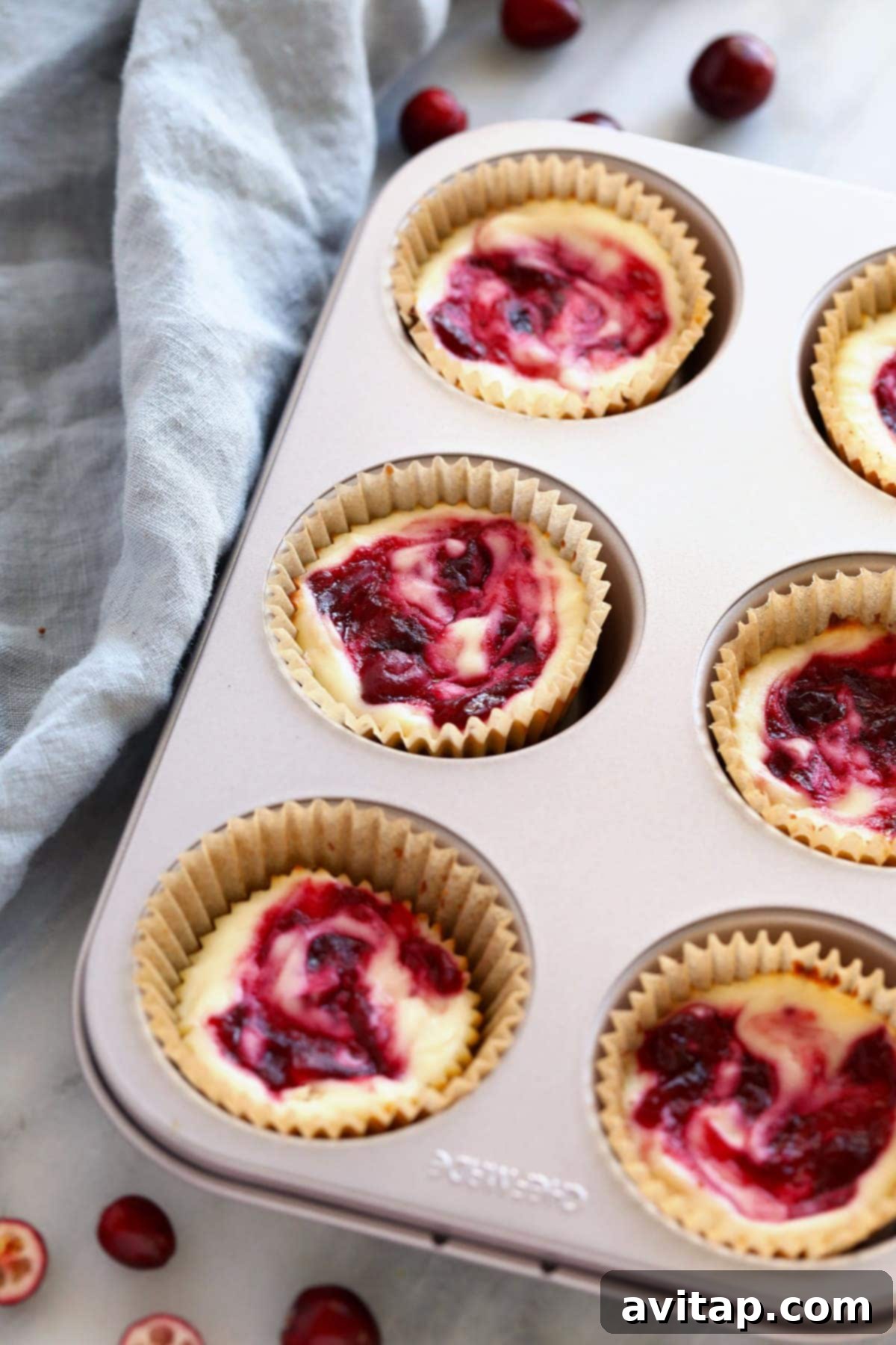 Cranberry cheesecakes in a muffin tin, freshly baked and ready to cool.