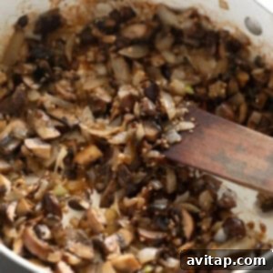 Sauteed mushrooms in a pan with a wooden spoon.