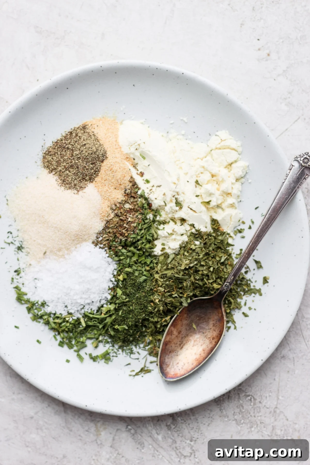 Freshly prepared ranch spices artfully arranged on a plate, featuring dried buttermilk, parsley, dill, chives, garlic powder, onion powder, salt, and pepper, ready for mixing and use.