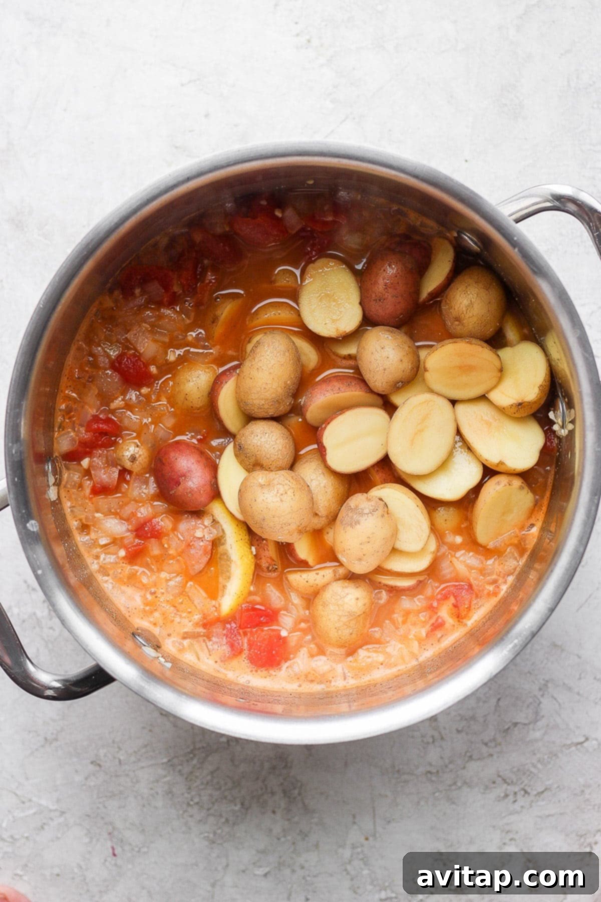Yukon gold potatoes being gently added to the richly seasoned, simmering seafood boil broth in a large stockpot.