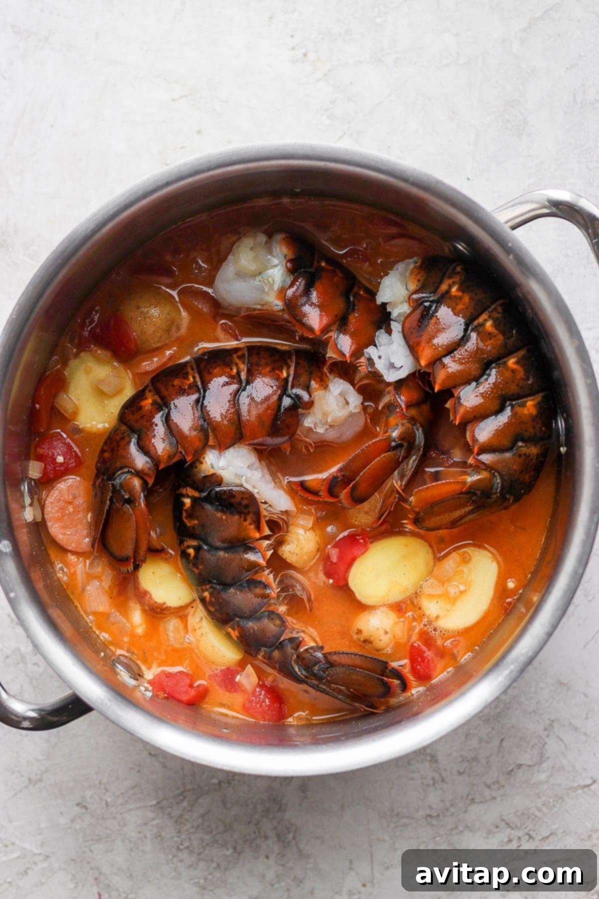 Fresh raw lobster tails being carefully placed into the bubbling, aromatic seafood boil broth.