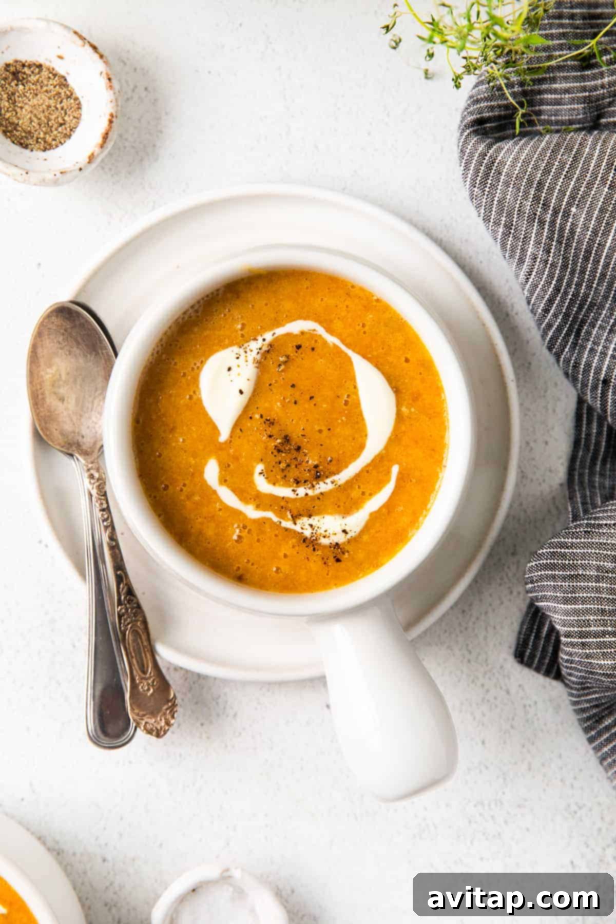 A vibrant bowl of creamy roasted butternut squash soup, beautifully garnished with a swirl of créme fraîche and a sprinkle of black pepper, ready to be enjoyed.