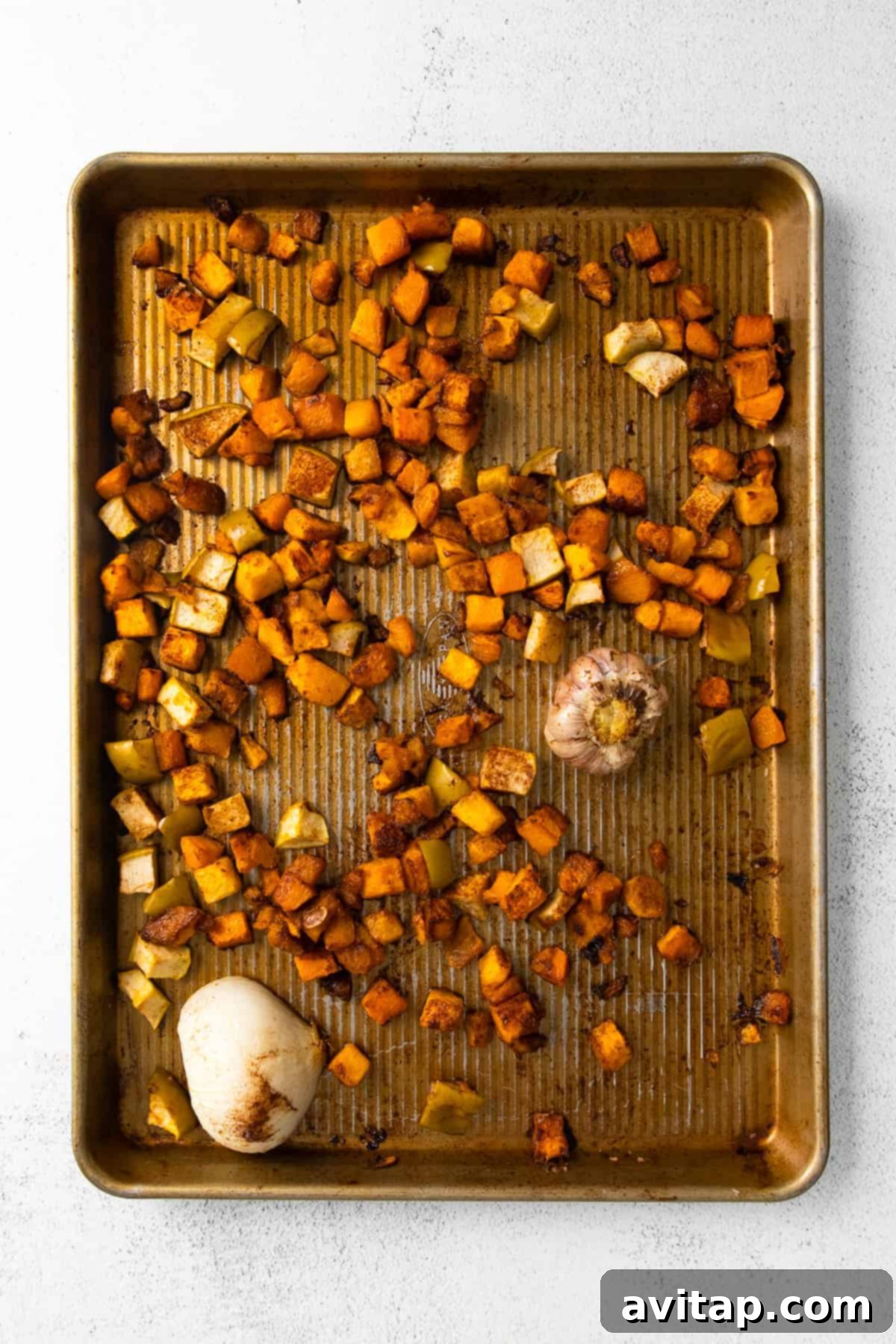 Perfectly roasted butternut squash, onion, apple, and garlic, golden brown and tender, displayed on a baking sheet straight from the oven.