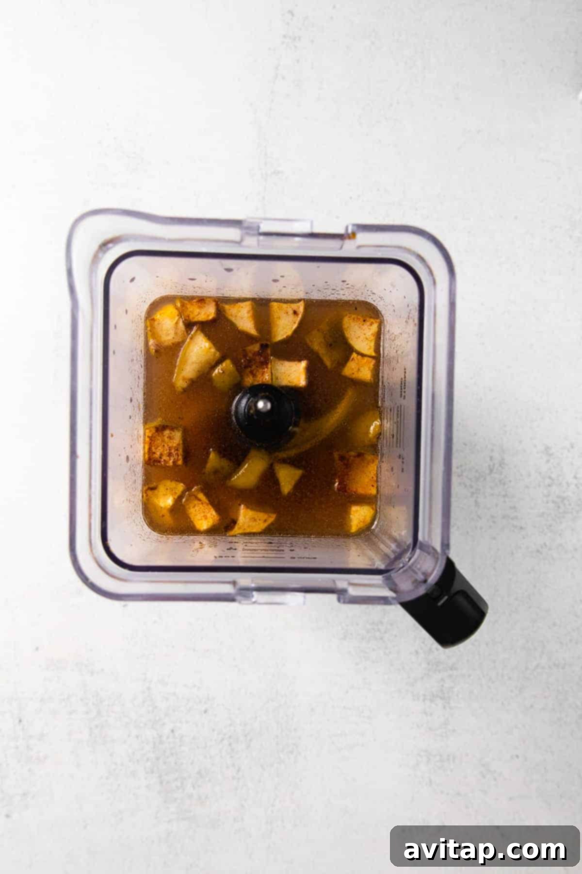 Roasted butternut squash, onion, apple, and garlic with broth being blended to a smooth, creamy consistency in a high-speed blender.