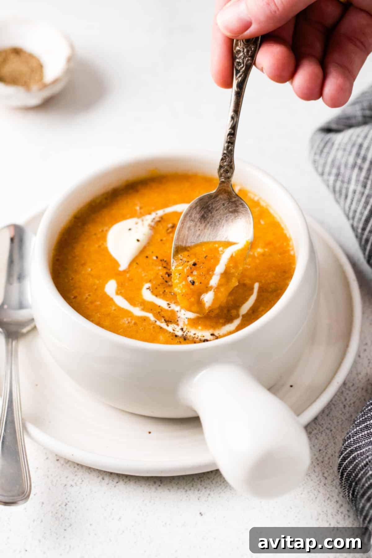 A beautifully presented bowl of creamy roasted butternut squash soup, garnished with créme fraîche and black pepper, set on a rustic wooden table, invitingly ready to eat.