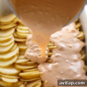 Pouring rich, creamy cheese sauce over layers of sliced potatoes in a casserole dish.