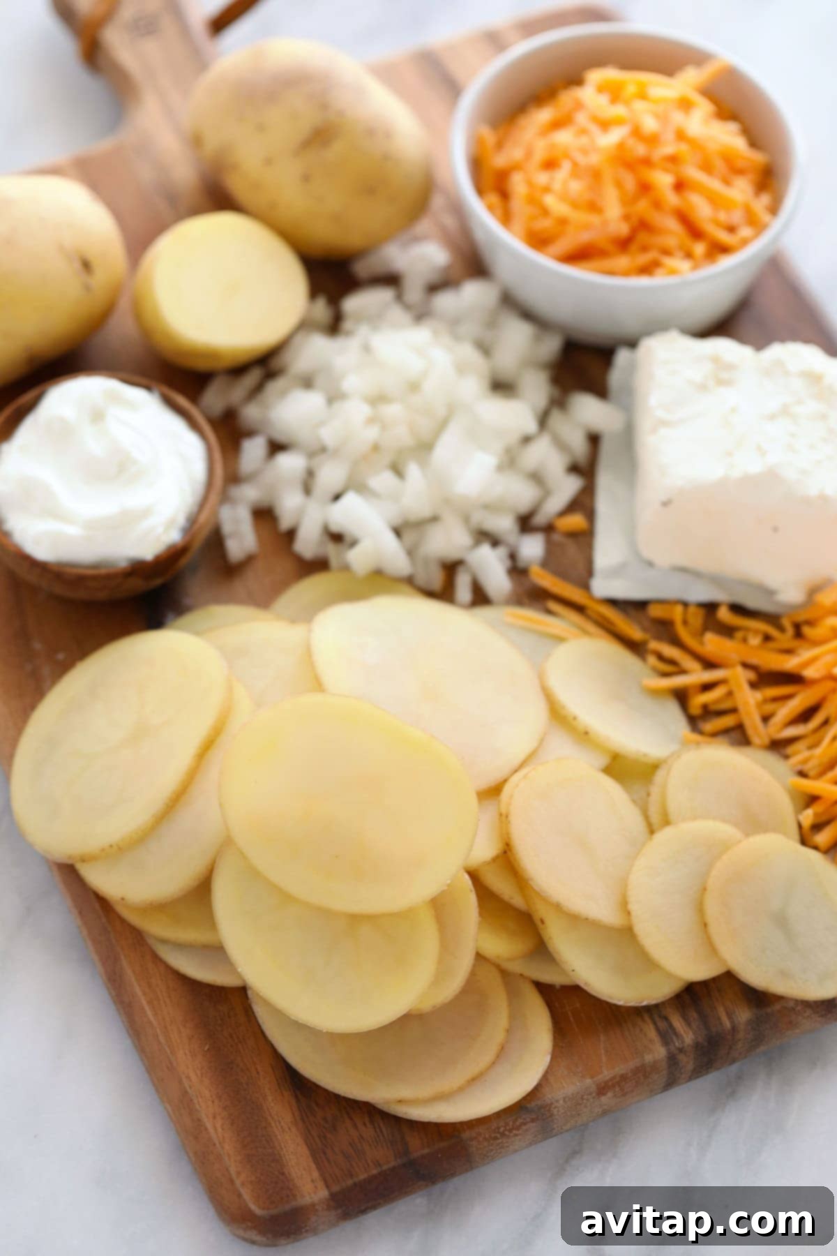 A selection of fresh ingredients including potatoes, garlic, and onions arranged on a wooden cutting board, ready for making scalloped potatoes.