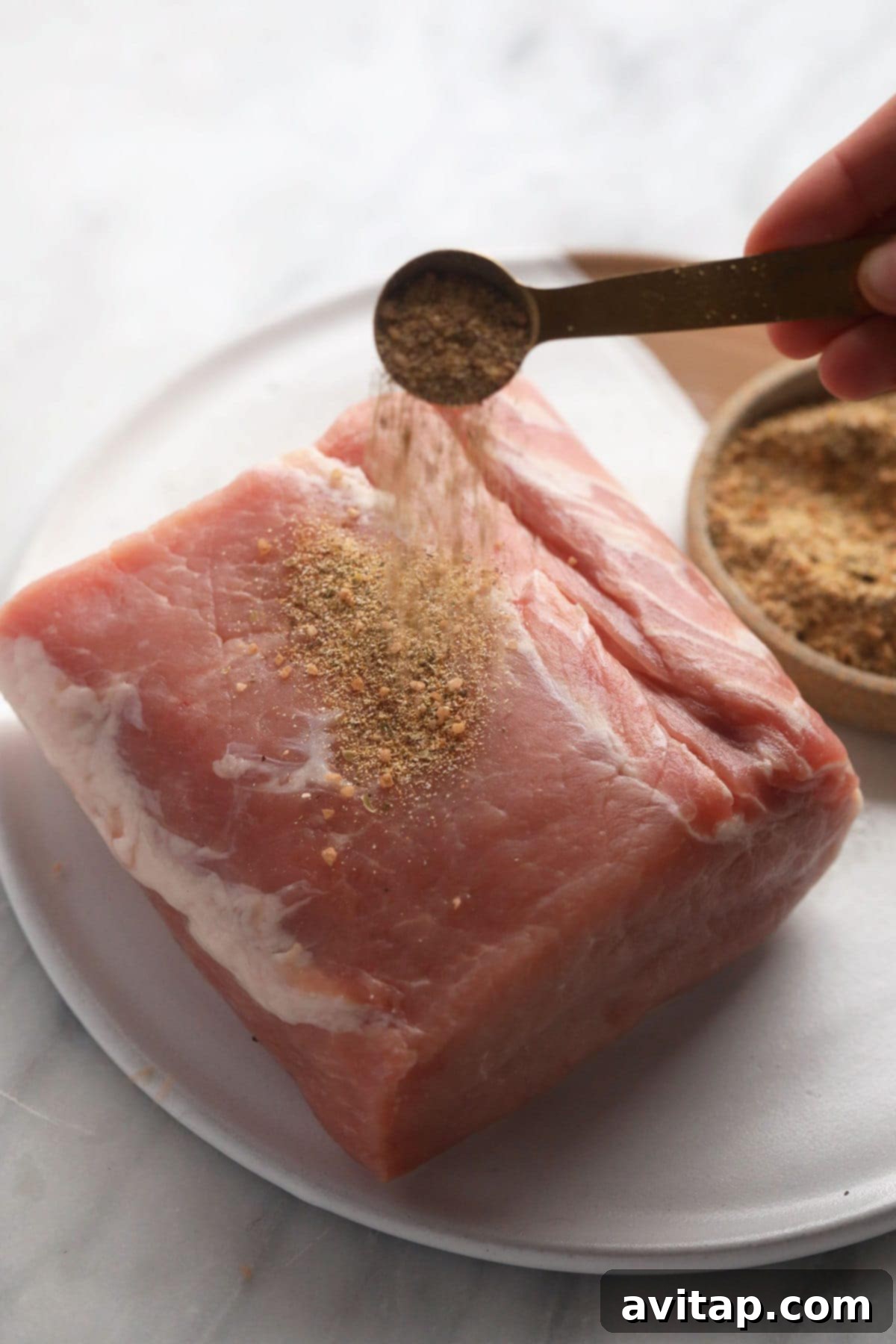 Raw pork loin roast being generously seasoned with a flavorful homemade pork dry rub, ready for searing.