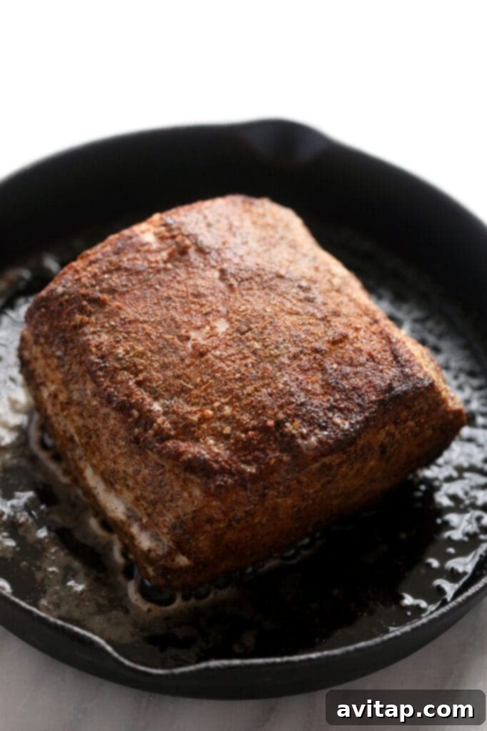 A beautiful pork loin roast achieving a perfect golden-brown crust as it sizzles in a hot cast iron skillet, a crucial step for enhanced flavor.