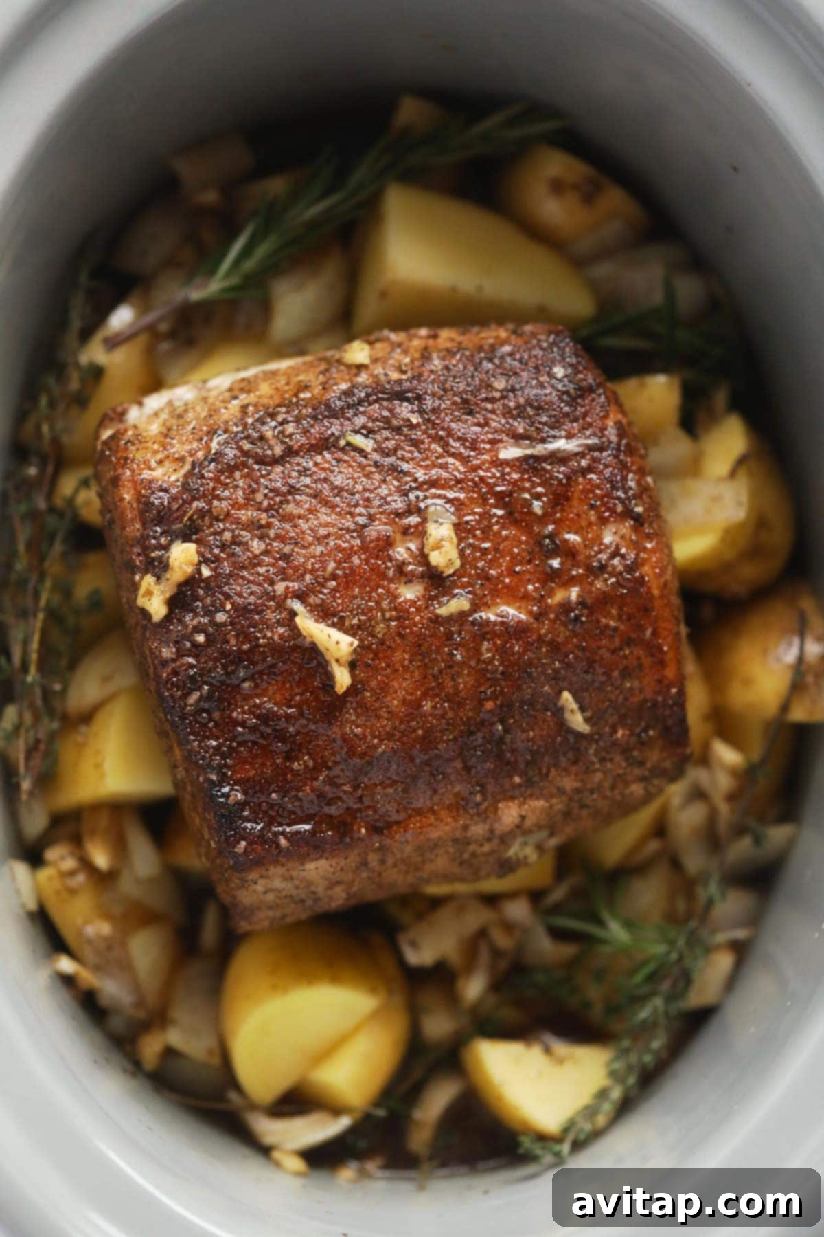 A slow cooker filled with a tender pork loin roast, surrounded by comforting potatoes and aromatic herbs, simmering to perfection.