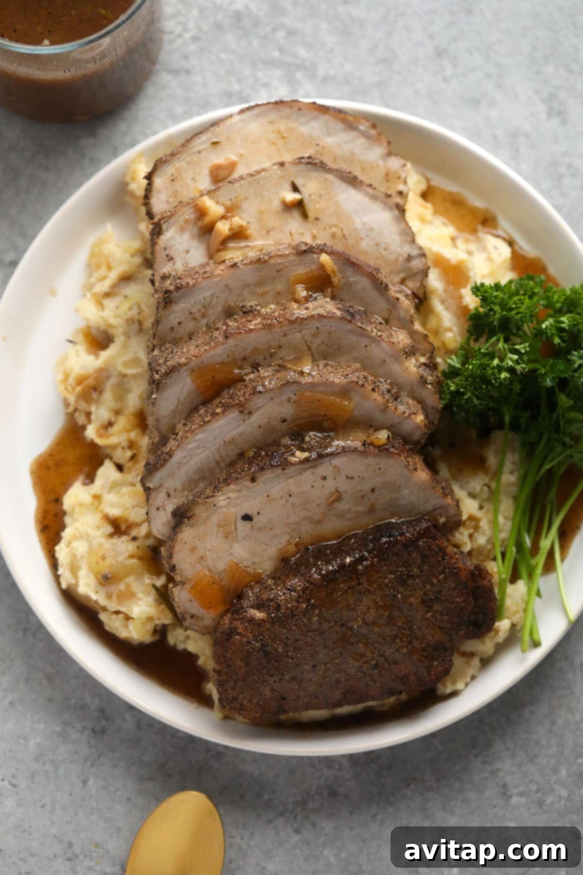 The finished slow cooker pork loin, beautifully sliced and presented on a generous bed of creamy mashed potatoes, lavishly covered in homemade savory gravy.