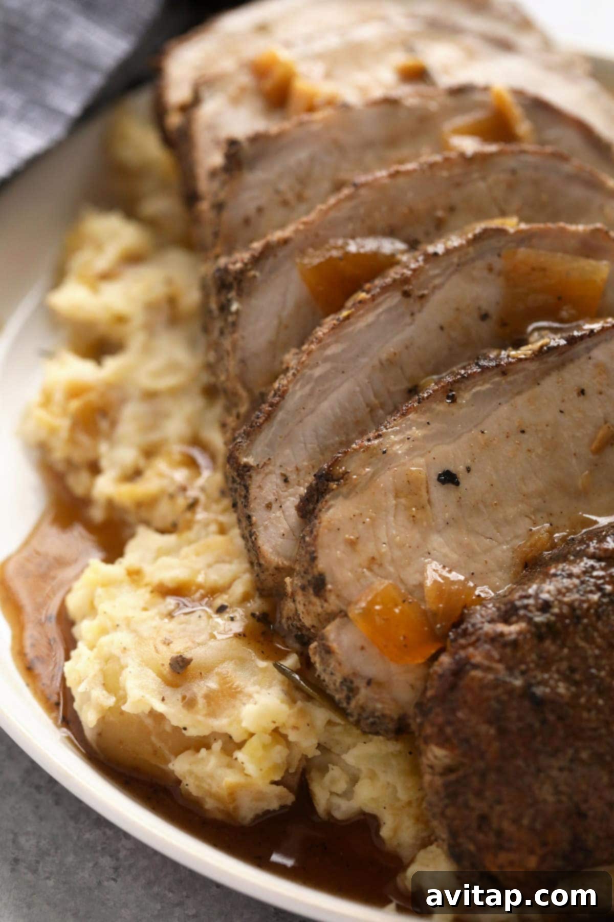 Perfectly sliced slow cooker pork loin, glistening with delicious savory gravy, ready to be served and enjoyed.