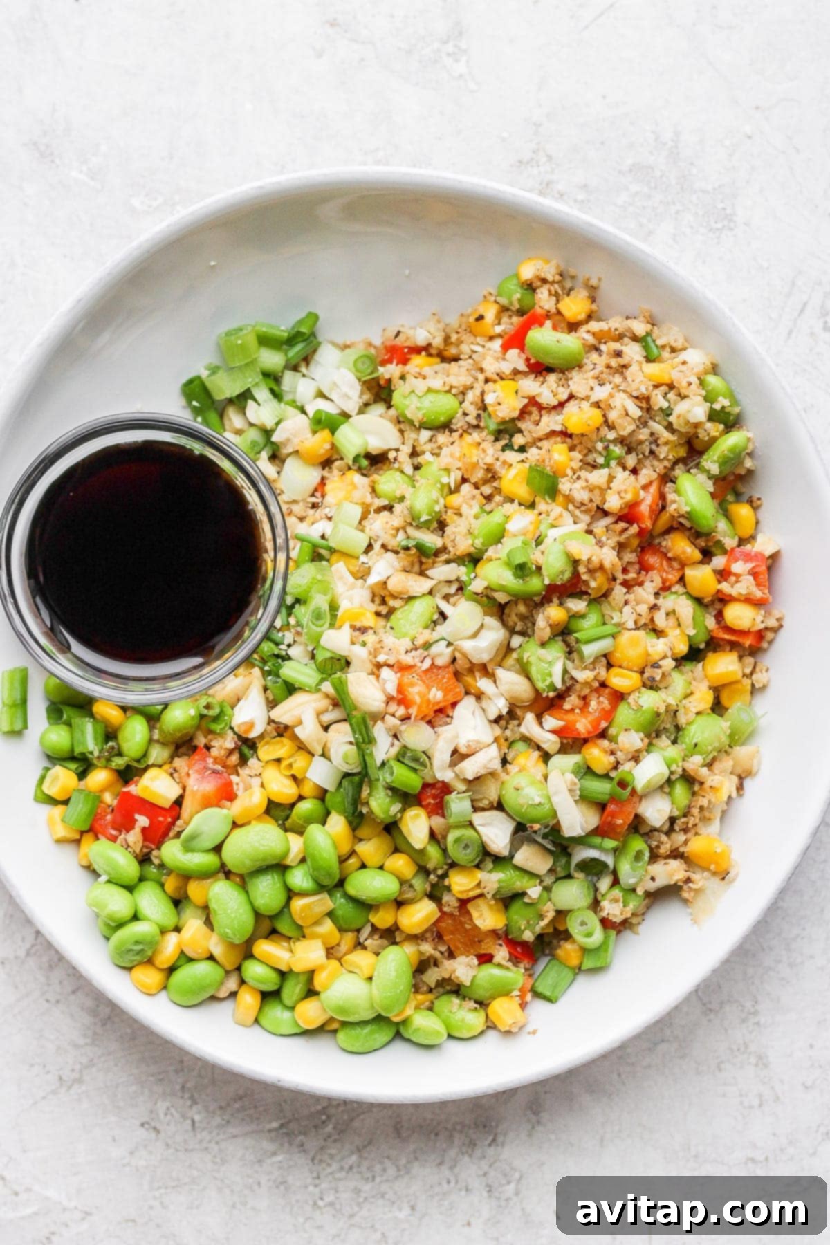 A bowl of freshly prepared cauliflower fried rice served alongside a small dish of savory sauce, ready to be enjoyed.