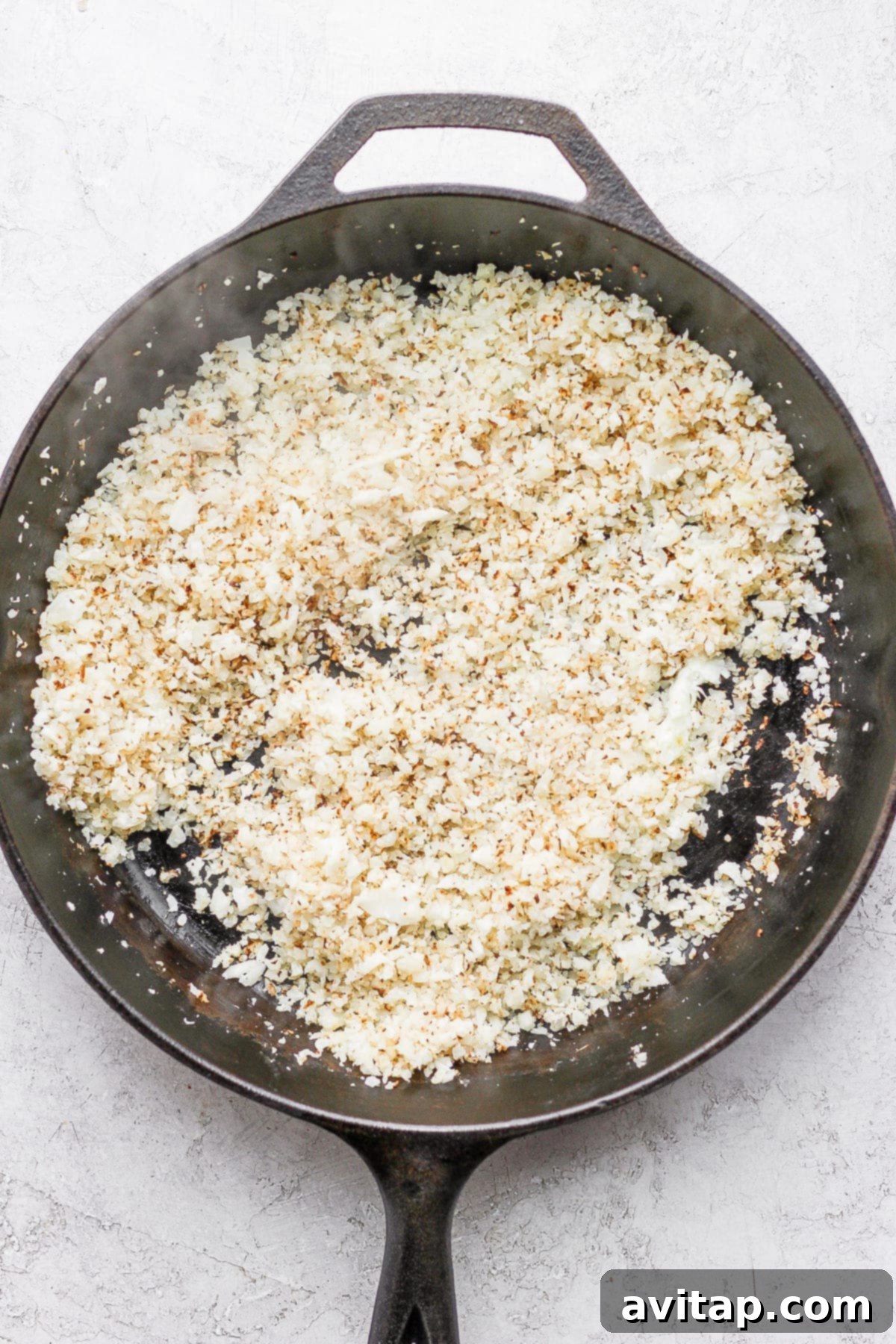 Finely riced cauliflower being sautéed in a hot skillet, beginning to brown and release its aromatic flavors.