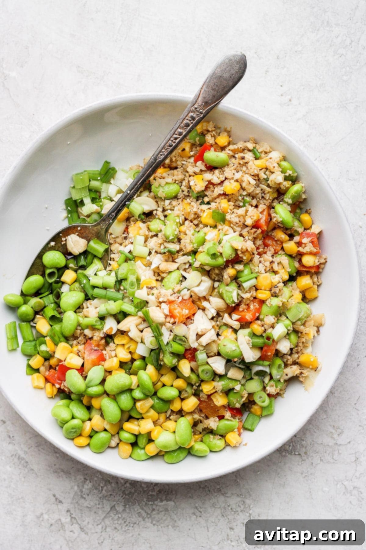 A beautifully presented bowl of cauliflower fried rice, garnished with fresh green onions and chopped cashews, ready to be eaten.