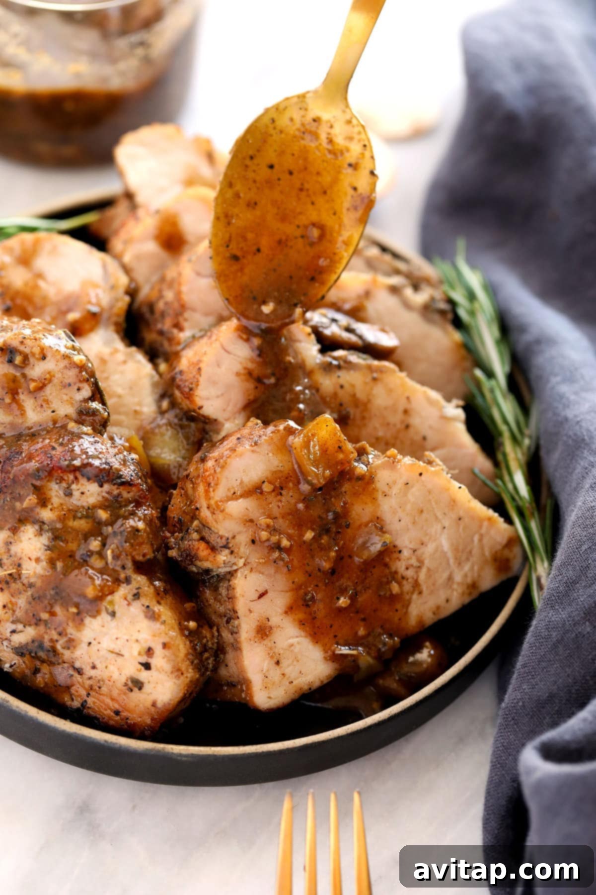 Sliced baked pork tenderloin being drizzled with rich mushroom gravy.