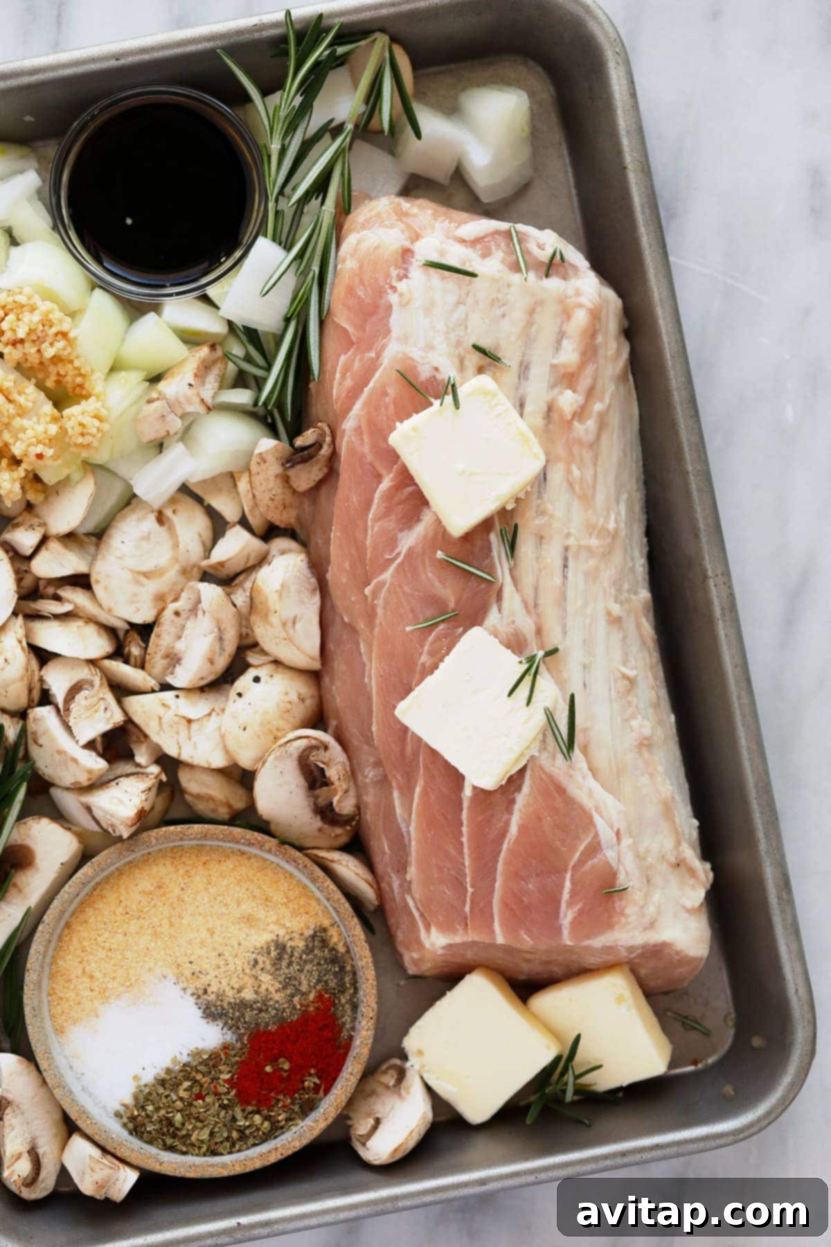Raw pork tenderloin seasoned and ready for cooking with mushrooms and butter on a sheet pan.