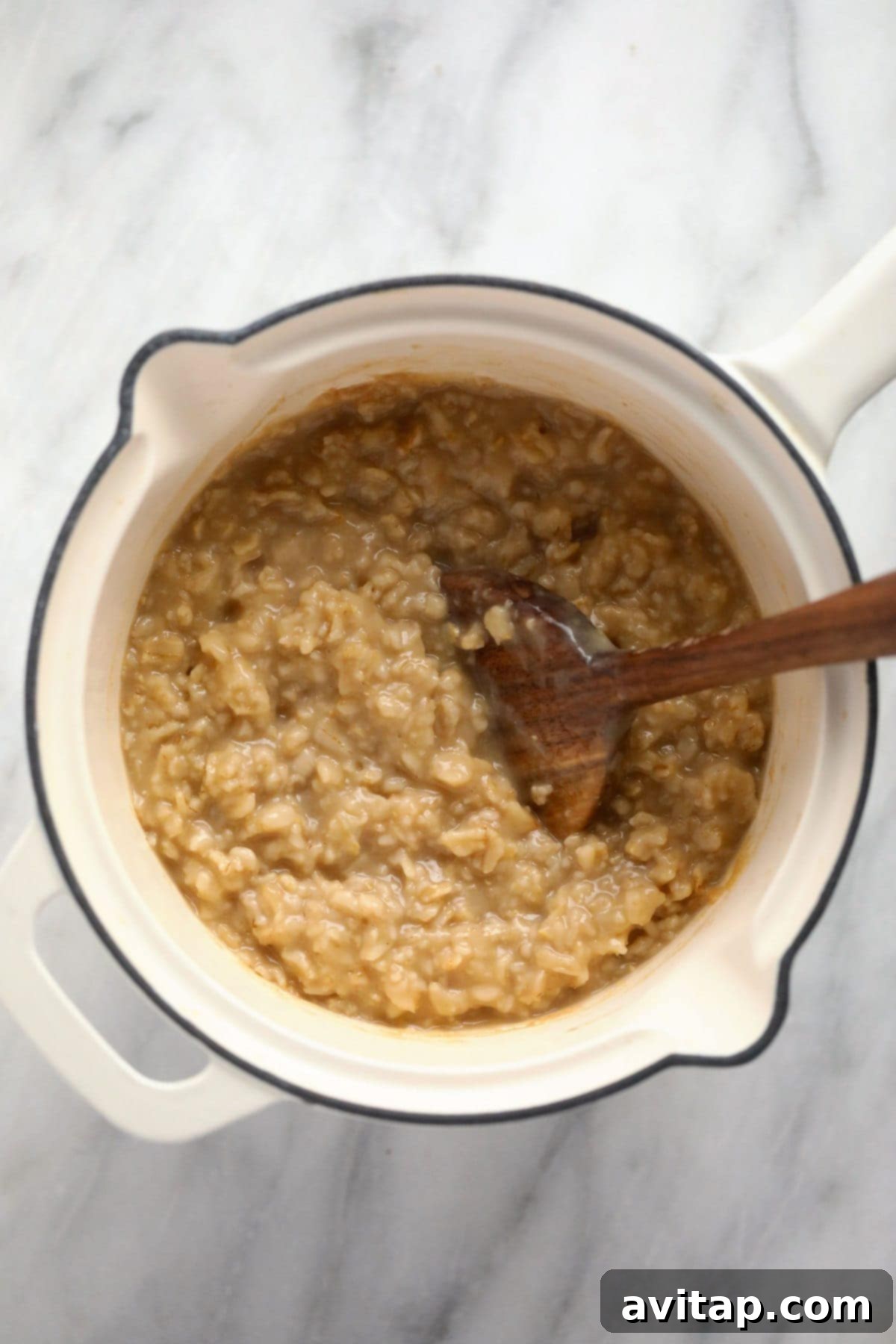 Delicious Savory Oatmeal 5 Rich, creamy savory oatmeal gently simmering in a small pot, stirred with a wooden spoon, achieving the perfect consistency for a comforting and wholesome meal.