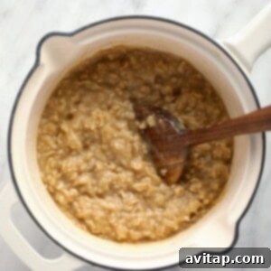 Oatmeal cooking in a pot with a wooden spoon, becoming creamy.