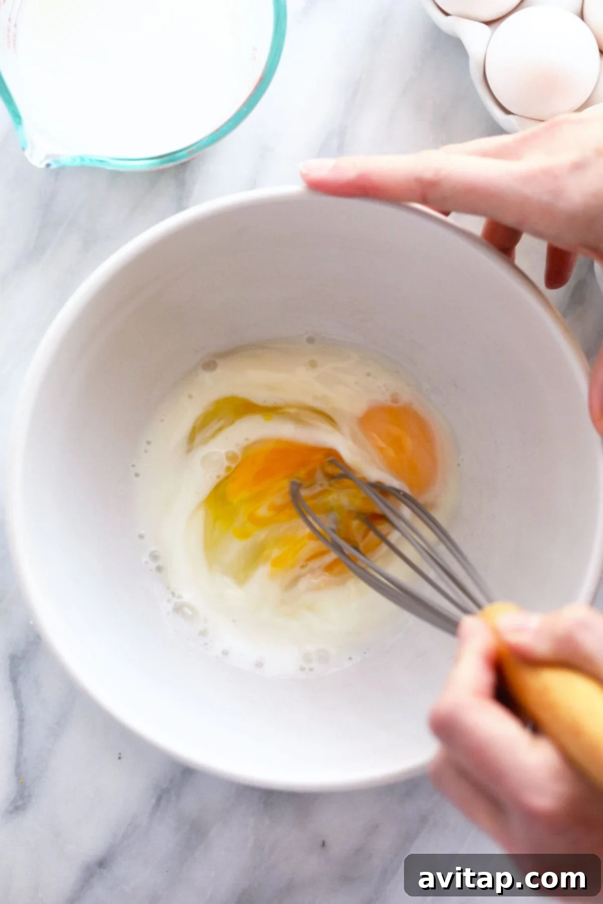 Whisked Eggs and Milk in Bowl Raw eggs and milk perfectly combined in a bowl, ready to be poured into the skillet, illustrating the initial stage of preparing scrambled eggs.