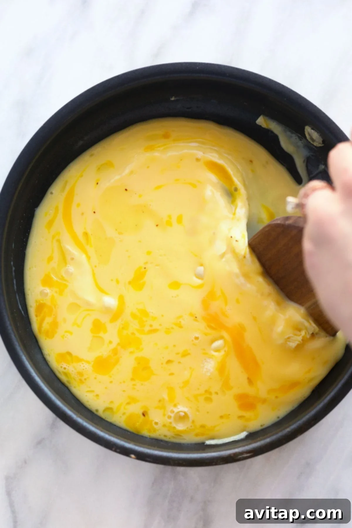 Scrambled Eggs Cooking in Pan Scrambled eggs gently cooking in a non-stick pan, being stirred with a wooden spatula to create soft, fluffy curds.