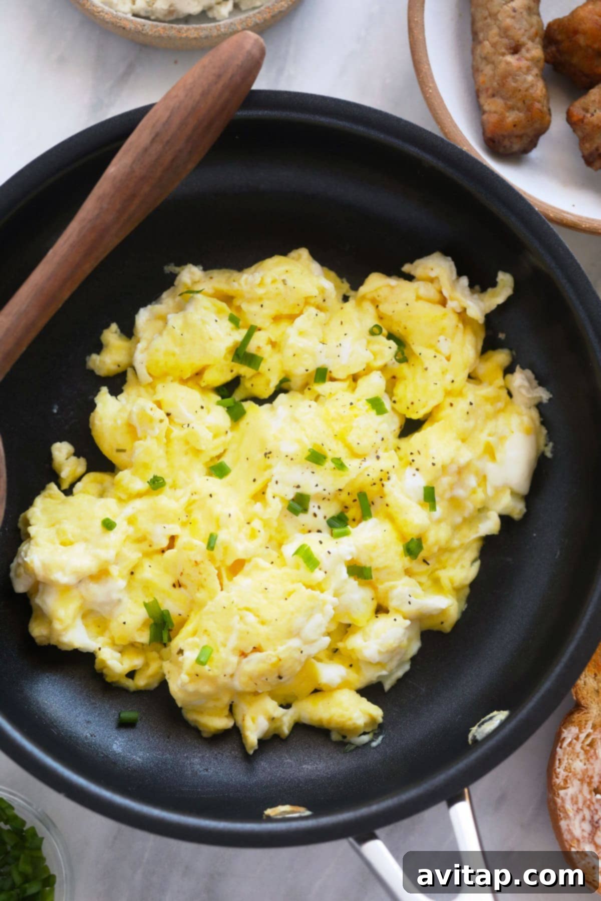 Scrambled Eggs with Chives A serving of perfect scrambled eggs in a skillet, garnished with fresh chopped chives, ready to be enjoyed.