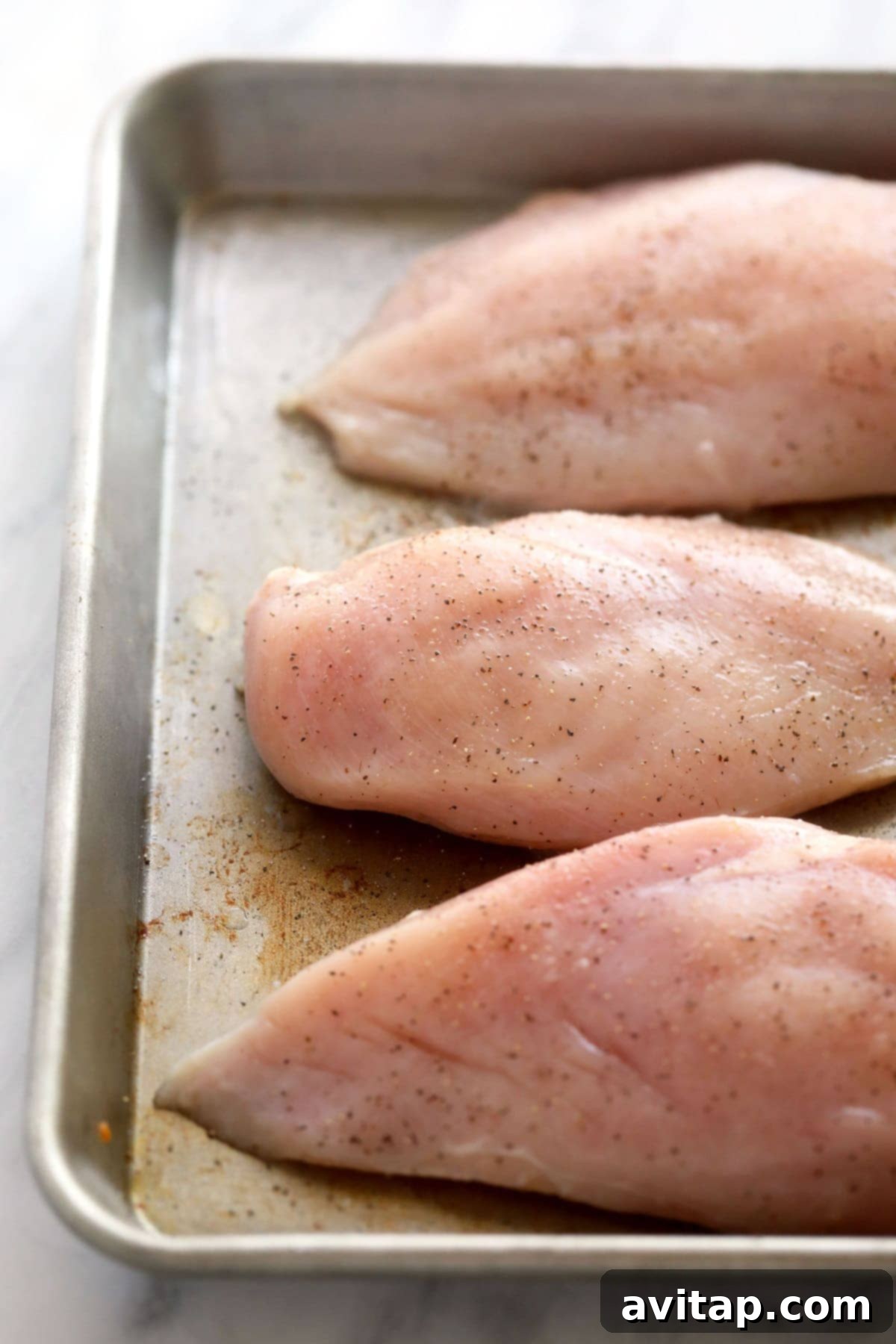 Raw boneless, skinless chicken breasts arranged on a baking sheet, prepped and ready for baking to be transformed into tender shredded chicken.