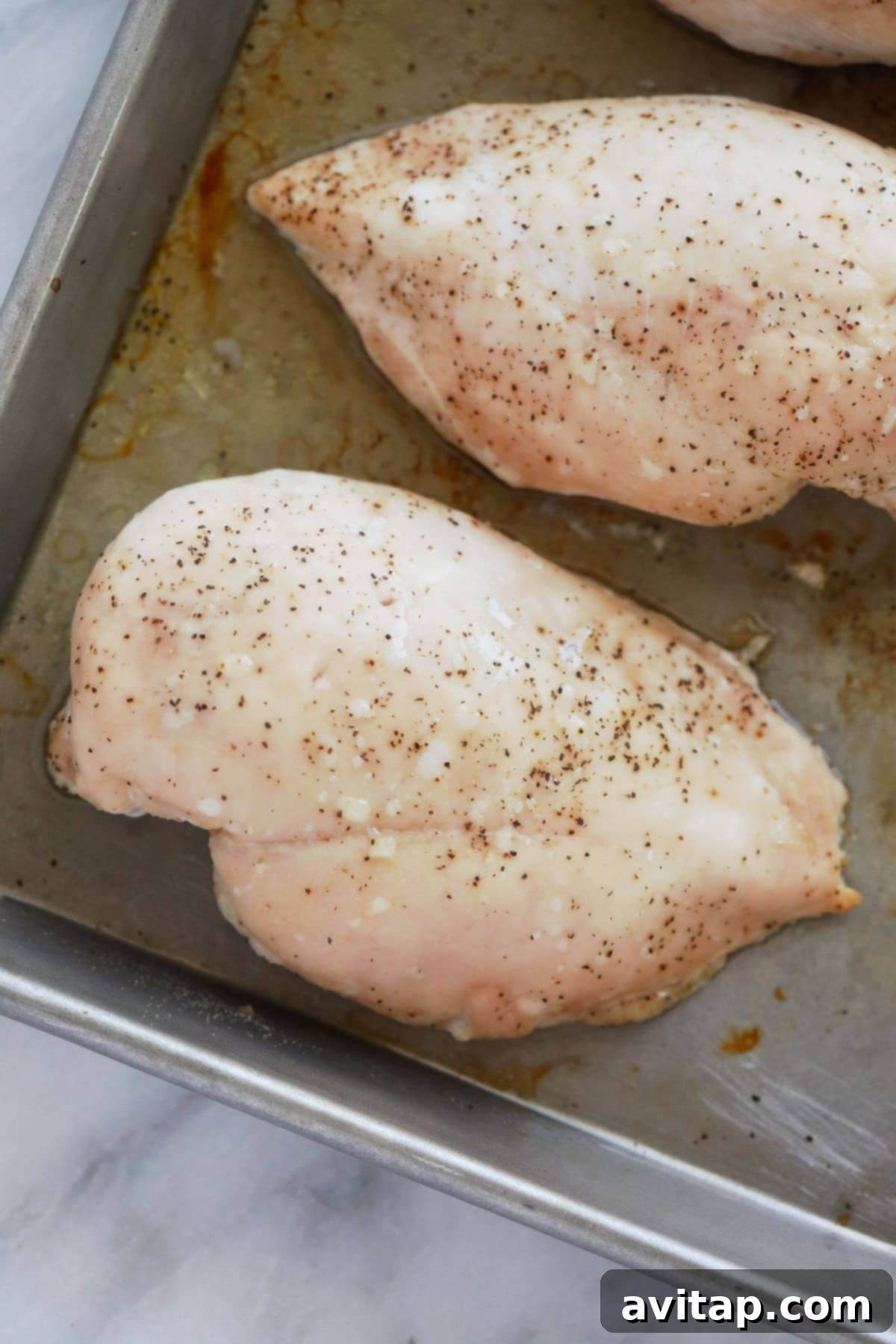 A perfectly baked chicken breast resting on a baking sheet after being removed from the oven, ready for the next step of shredding.
