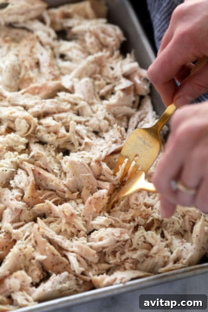 Close-up of a chicken breast being skillfully shredded with two forks on a cutting board, demonstrating a common shredding technique.