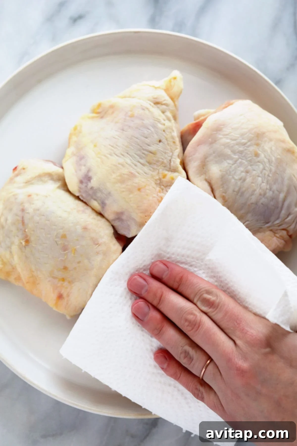 Oven-Fried Crispy Thighs 3 Hands patting down raw chicken thighs with a paper towel on a cutting board, preparing them for cooking.