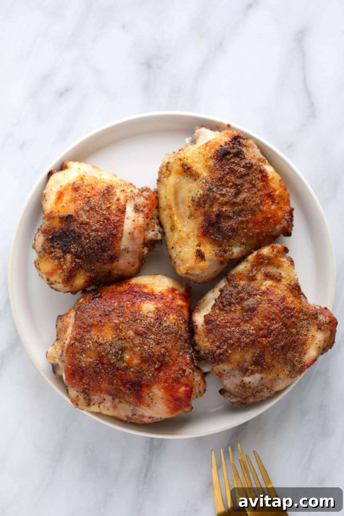 Oven-Fried Crispy Thighs 9 Three perfectly baked chicken thighs arranged on a plate with fresh herbs, showcasing their crispy golden skin.
