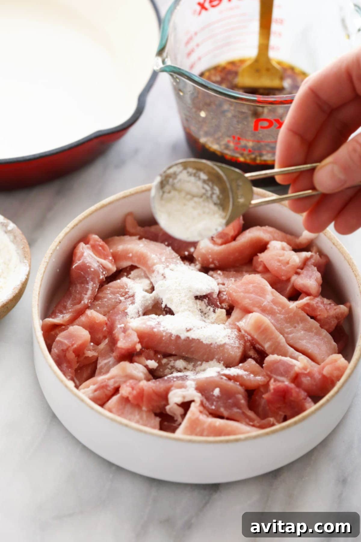 Pork strips being sprinkled with cornstarch, a step in preparing the sticky honey pork recipe.