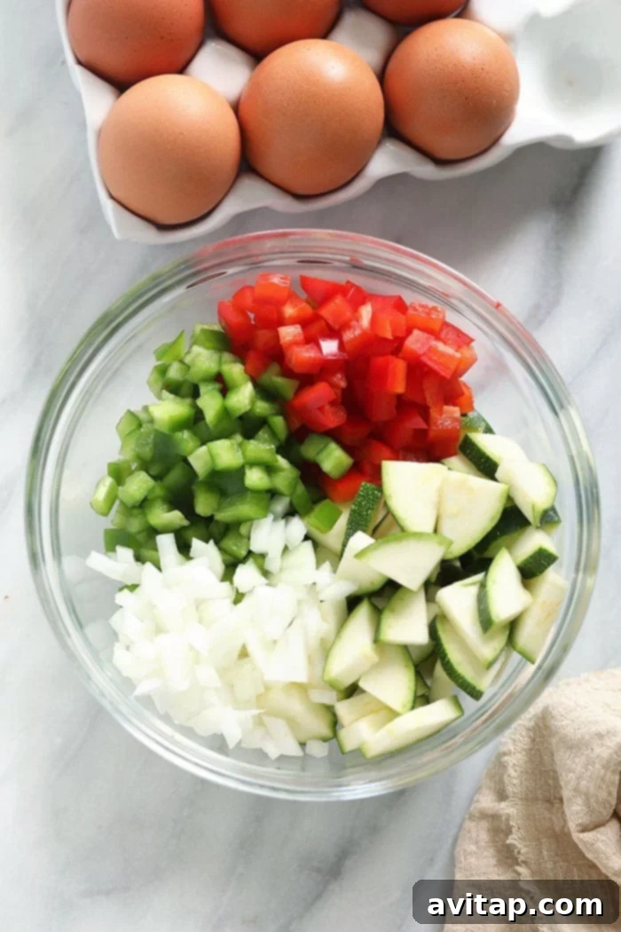 Freshly diced bell peppers, zucchini, and onions in a white bowl, ready to be sautéed for a delicious frittata.