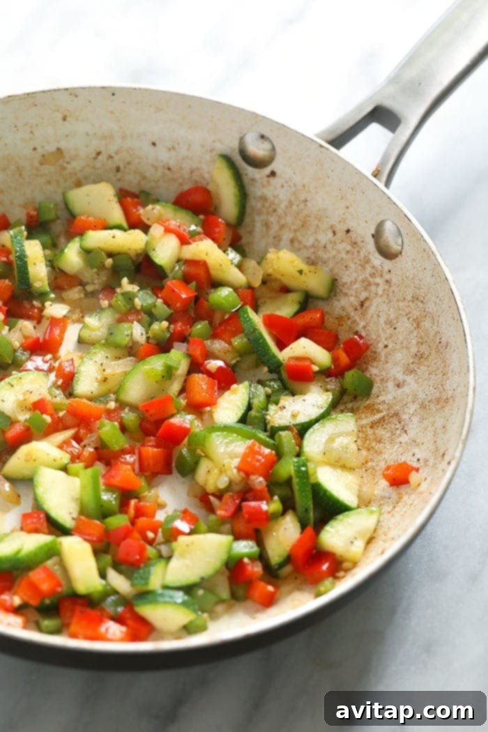 Colorful diced vegetables, including onions, bell peppers, and zucchini, perfectly sautéed in an oven-safe non-stick pan, ready for the egg mixture.