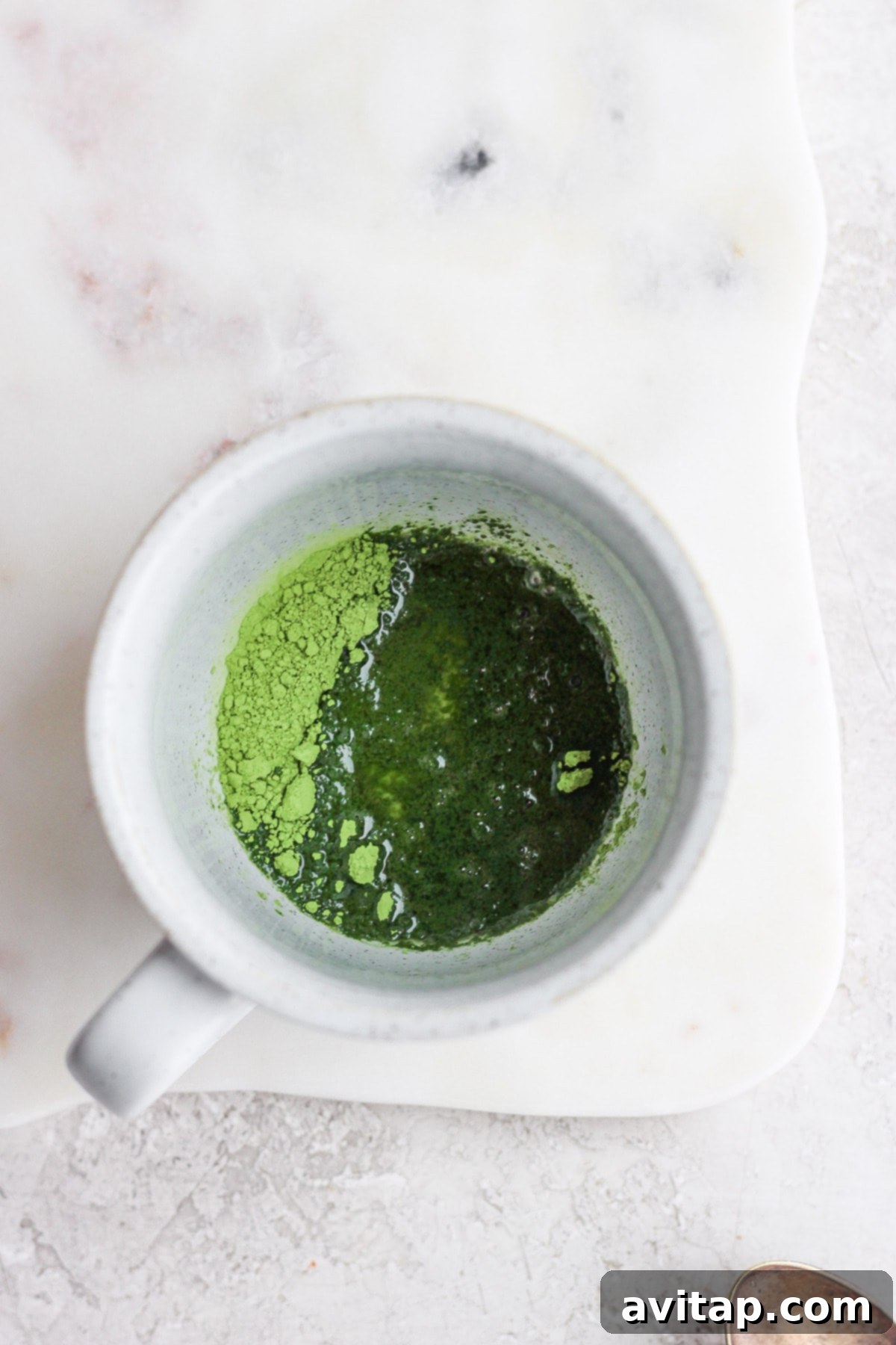Hot water being poured over vibrant green matcha powder in a mug, beginning the process of making a matcha latte.