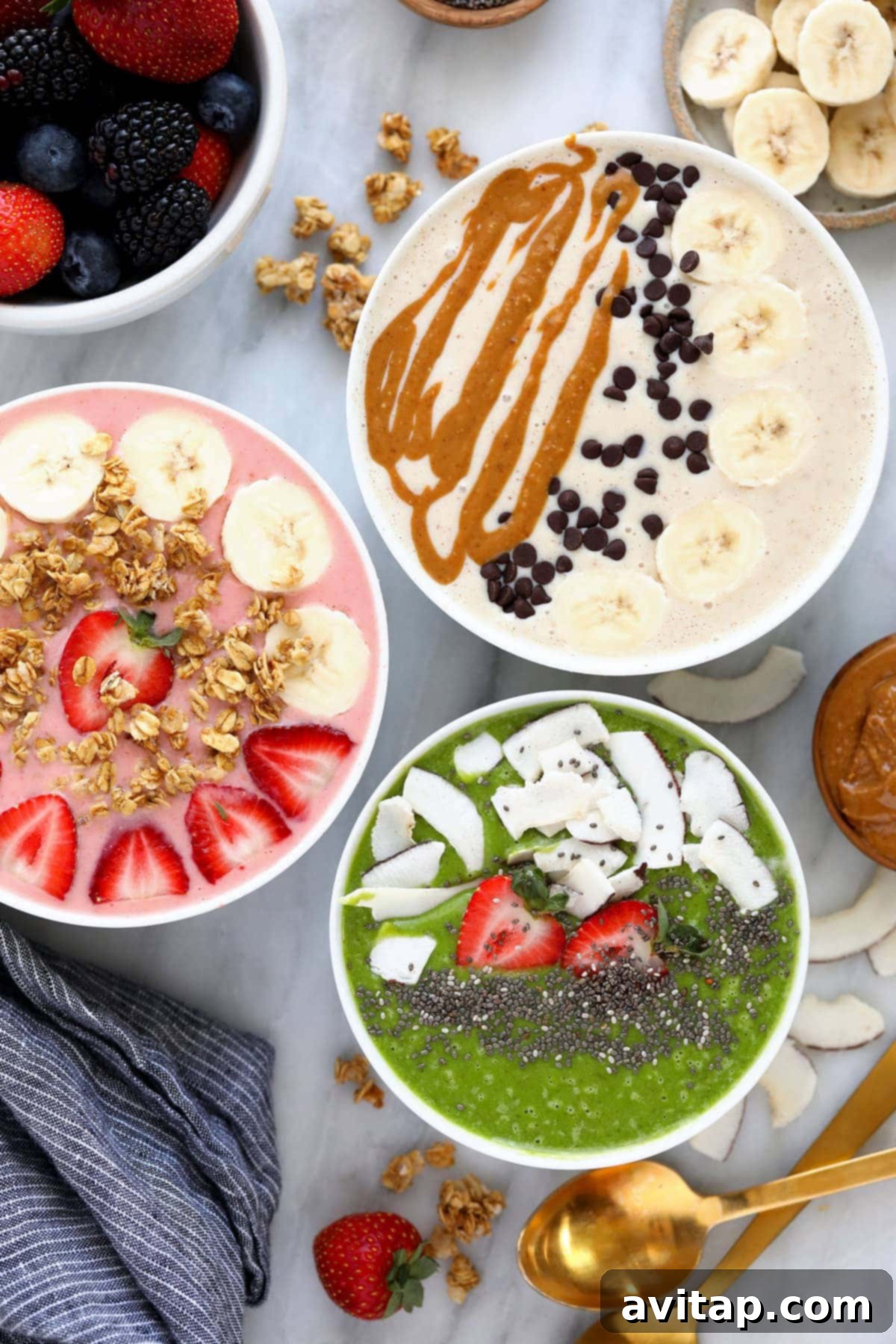 Three colorful and artfully arranged smoothie bowls, topped with fresh fruit, granola, and seeds, awaiting enjoyment.