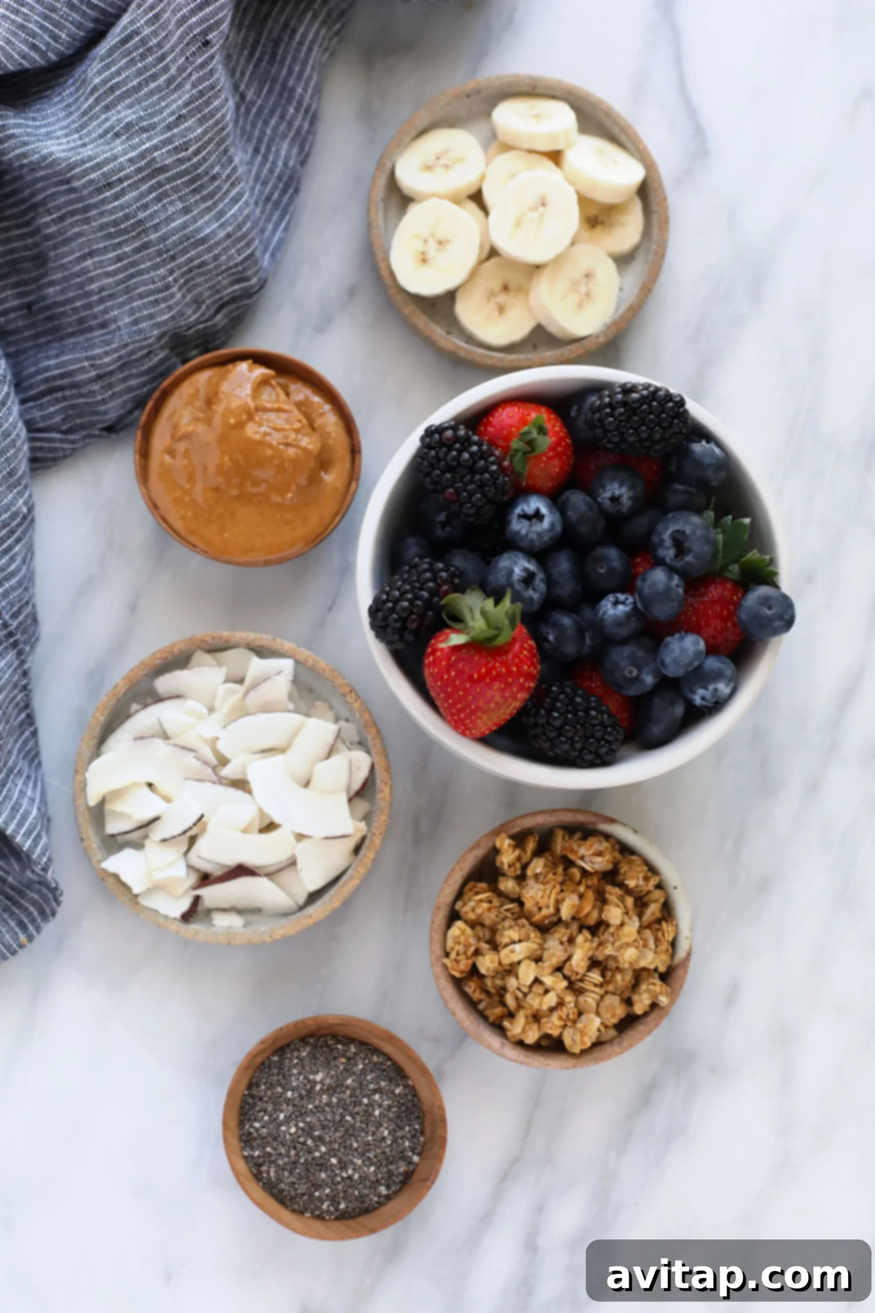 A beautiful arrangement of smoothie bowl toppings: fresh red berries, a swirl of creamy peanut butter, delicate coconut flakes, crunchy granola, and tiny chia seeds.