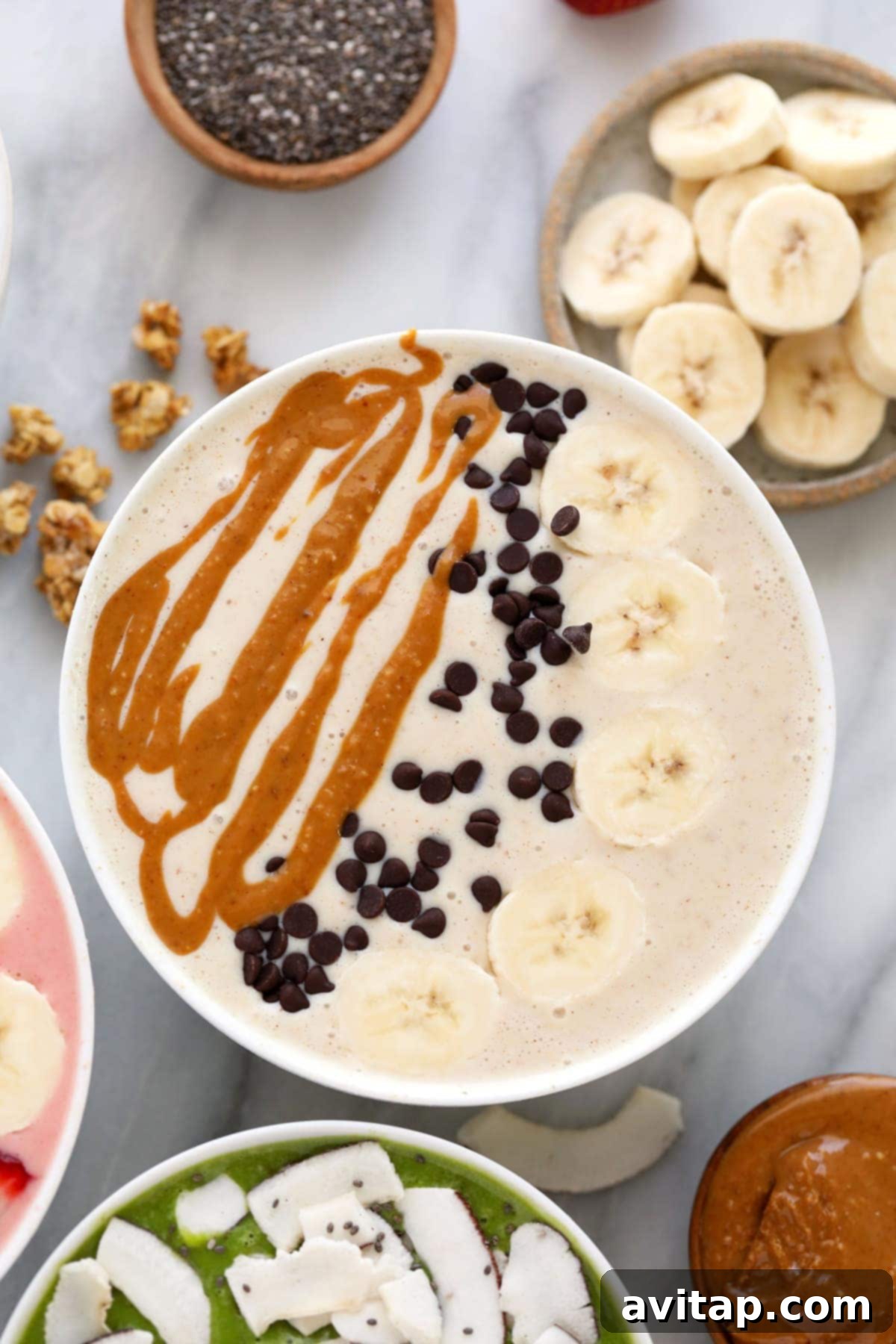 A creamy peanut butter banana smoothie bowl, beautifully topped with mini chocolate chips, fresh banana slices, and a luscious swirl of peanut butter.