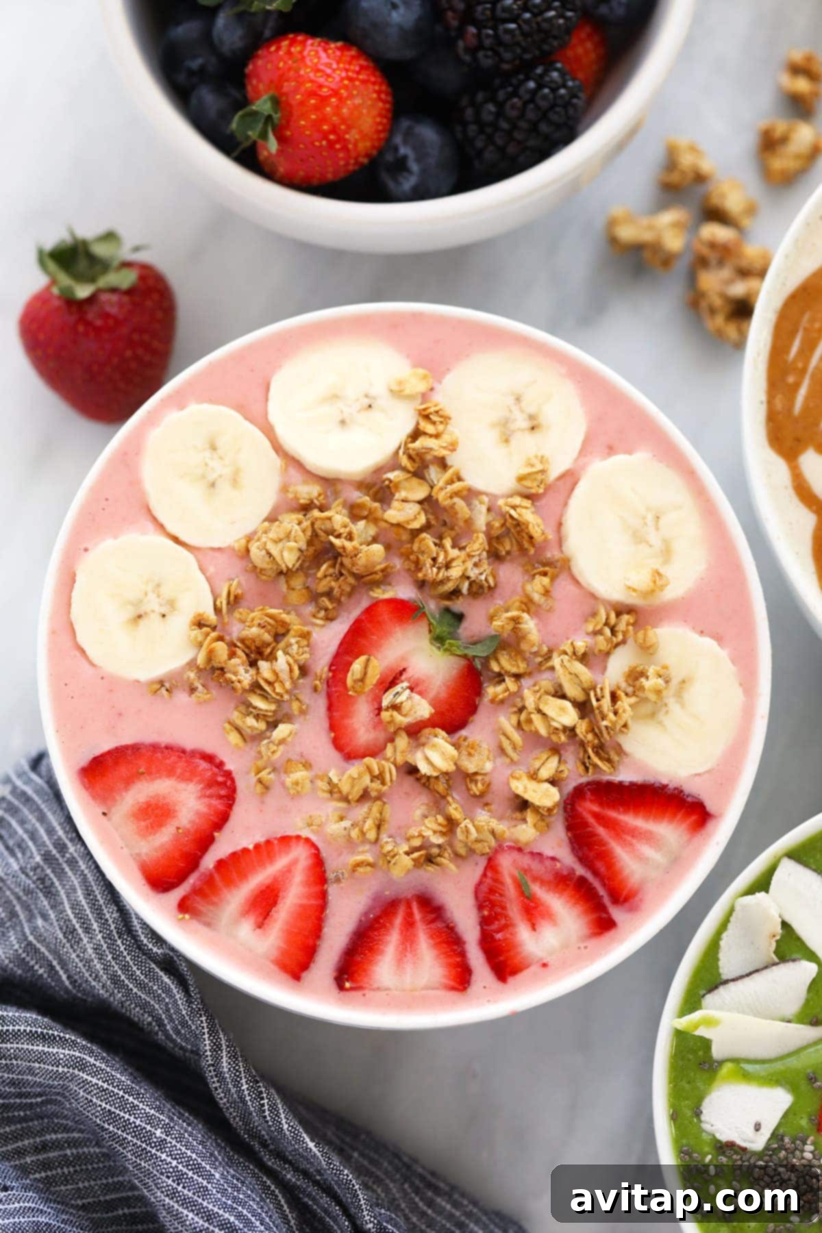 A refreshing strawberry smoothie bowl topped with crunchy granola, fresh banana slices, and whole strawberries.