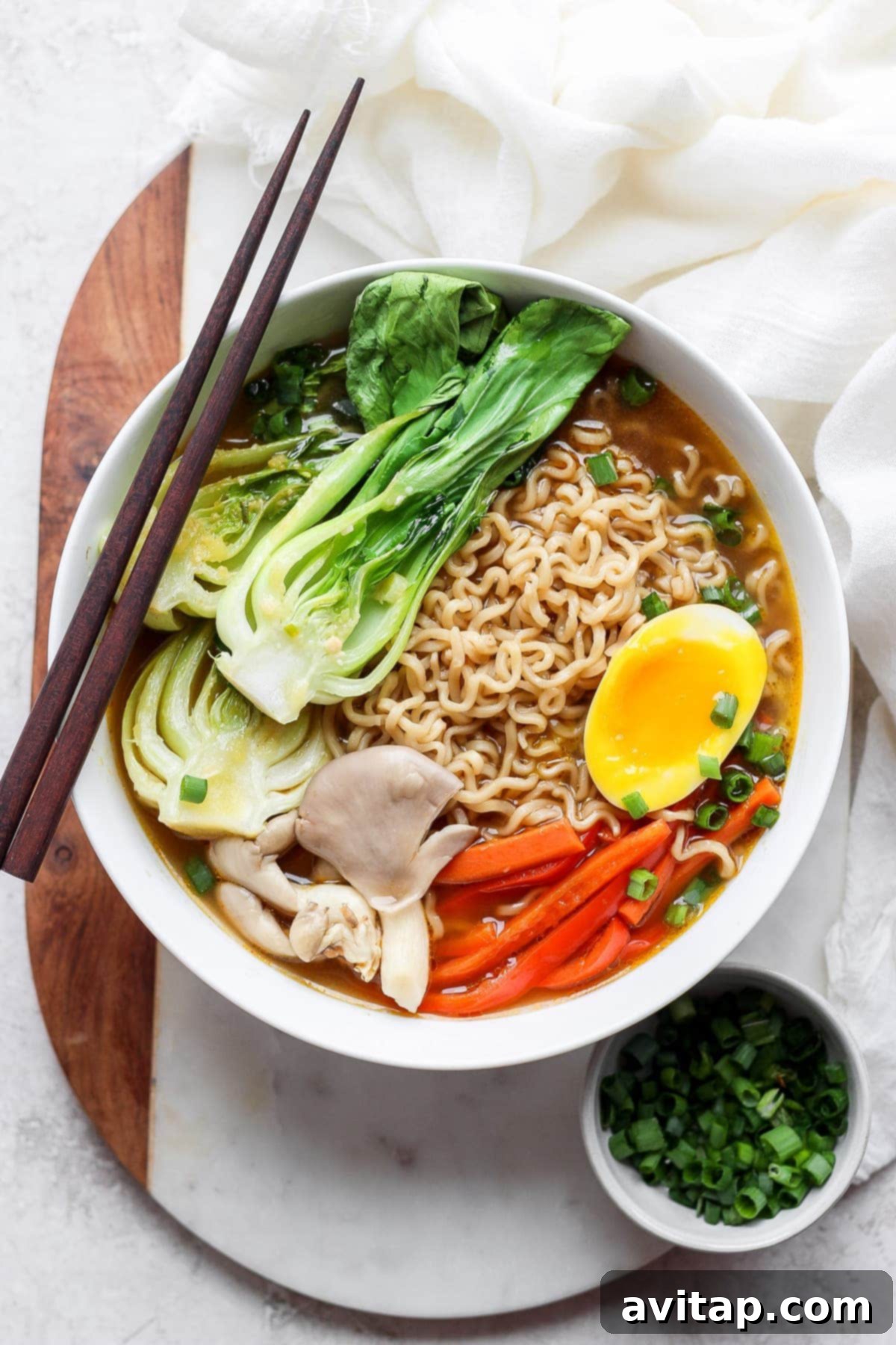 A beautifully presented bowl of vegetarian ramen with a soft-boiled egg, surrounded by fresh herbs and vegetables.