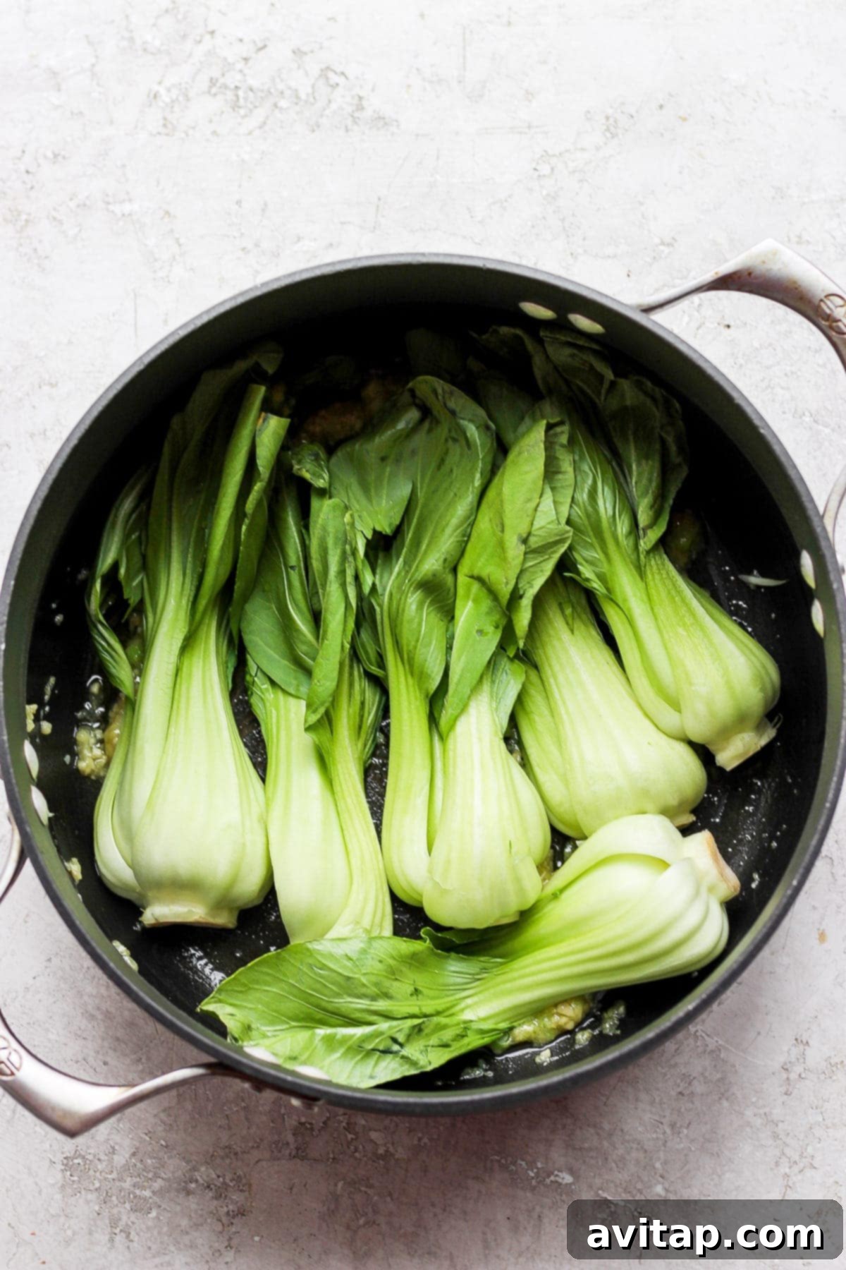 Tender bok choy cooking in a pot with garlic and ginger, soaking up all the aromatic flavors for a delicious ramen topping.