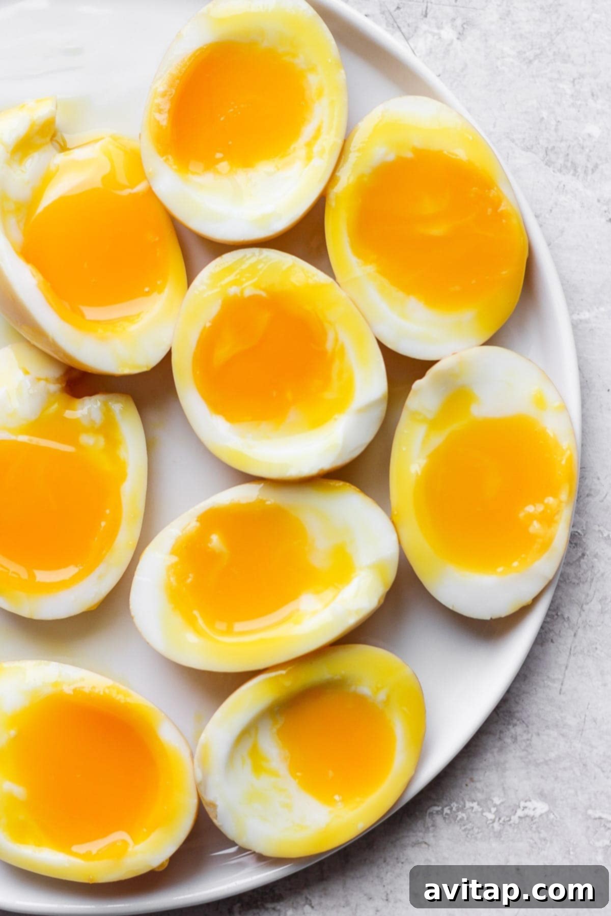Perfectly soft-boiled ramen eggs, halved, showcasing their creamy, jammy yolks and dark, marinated whites, served elegantly on a plate.